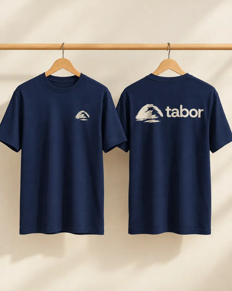 Duas camisetas azul-marinho penduradas, com o símbolo e o nome Tabor em creme.